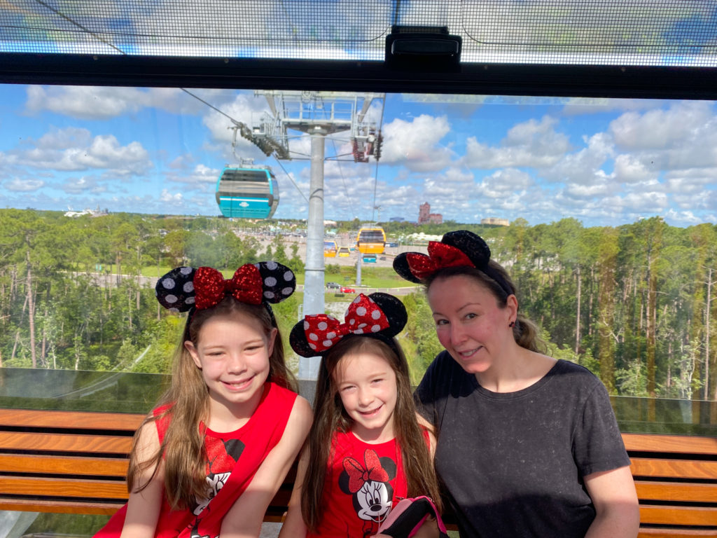 woman and two daughters with mouse ears riding in the Disney World Skyliner from Caribbean Beach Resort to Hollywood Studios