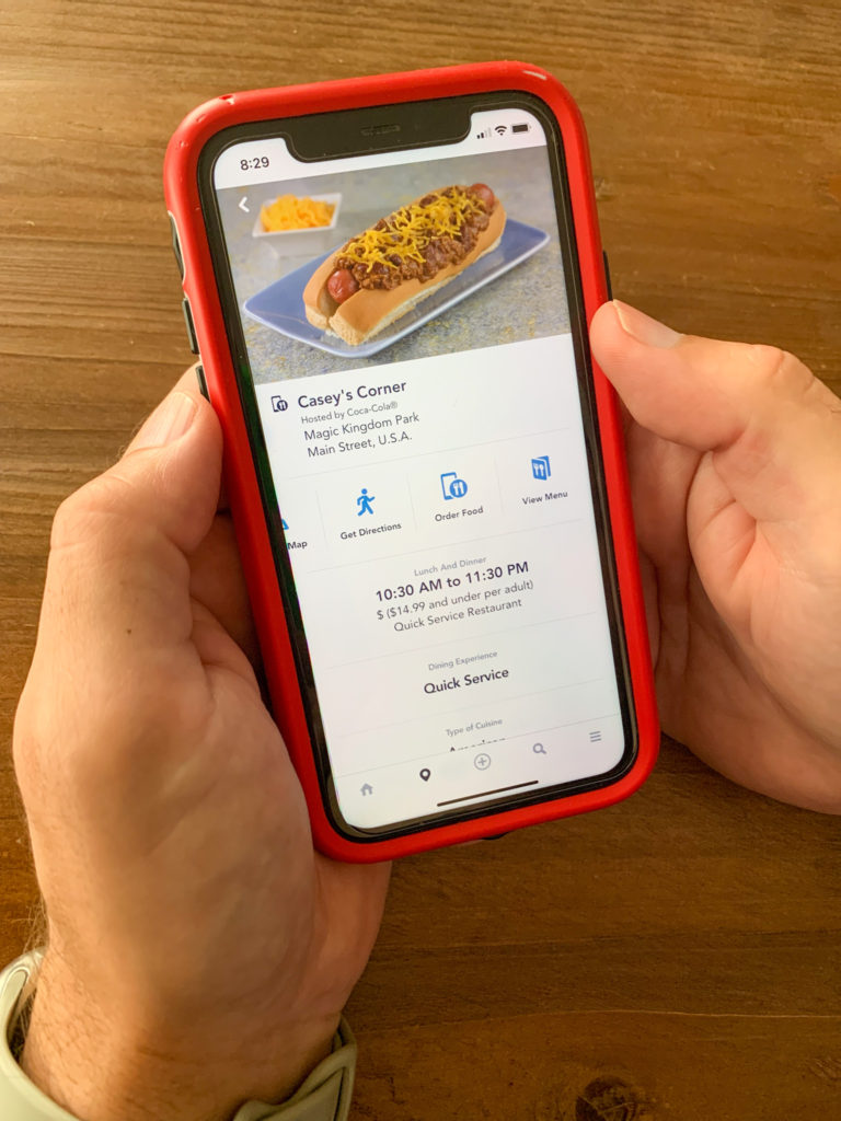 man holds phone with tips for first time at Disney using the Disney My Experience app to order quick dining meals