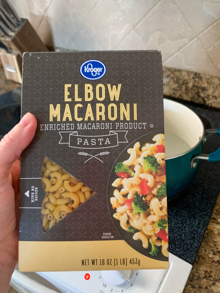 woman holds box of elbow pasta in front of stove 