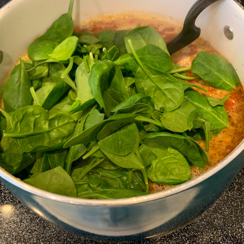 spinach piled on top of tortellini soup on stove in pot