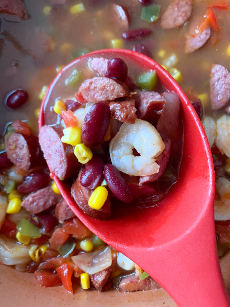 Cajun corn shrimp soup in red serving spoon over pot