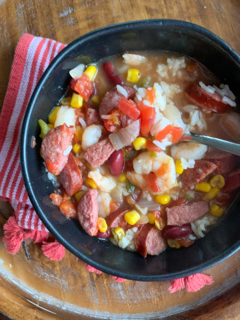 Cajun corn shrimp soup with rice in black bowl over red napkin