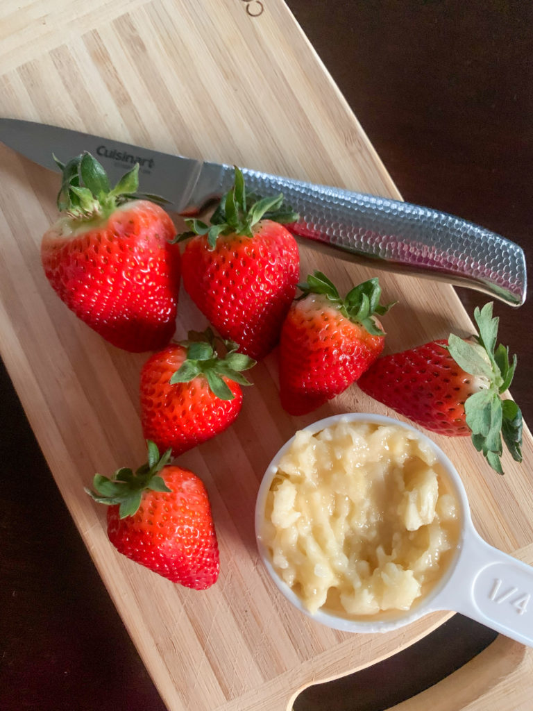 cutting board with strawberries and a measuring cup of mashed bananas with a knife