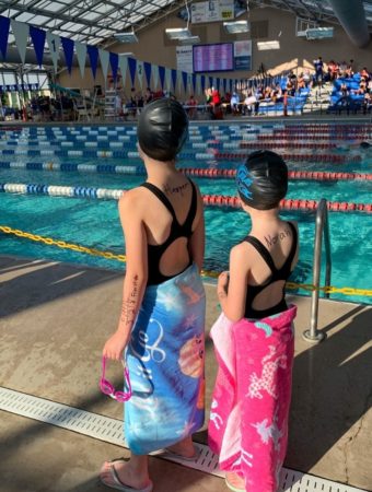 girls stand in front of competition pool at kids swim team meet event