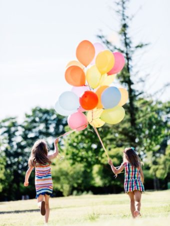 two sisters run with balloons at park birthday party