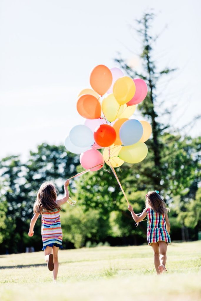 two sisters running with balloons at a playground party at the park
