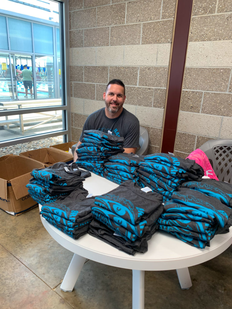 man smiles with pile of t-shirts