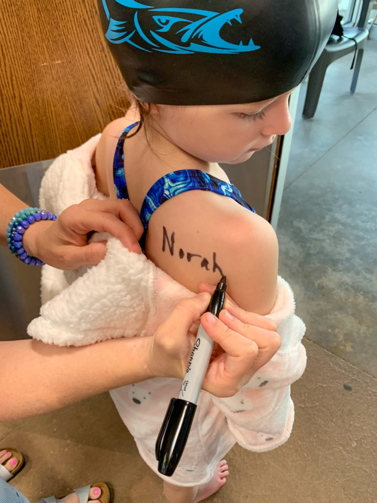 woman marks on child's shoulder with marker for kids swim meet