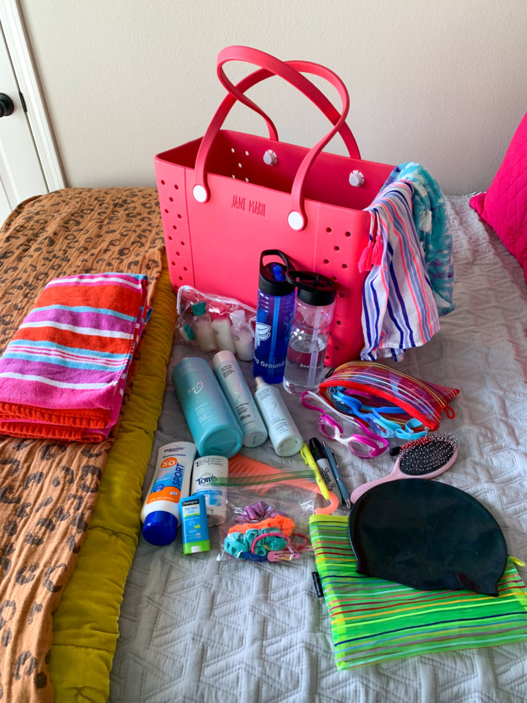 woman's swim team bag with accessories laid out on bed