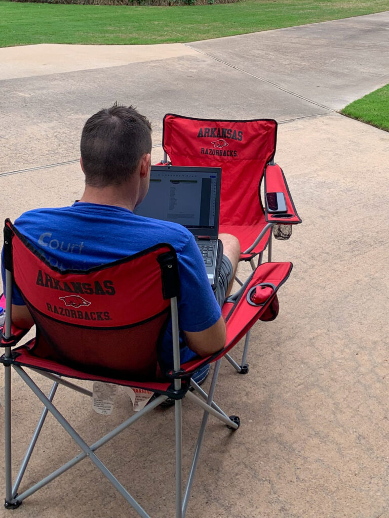 man sits in Arkansas Razorback lawn chair while working on a laptop