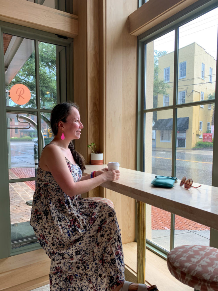 woman wears floral maxi dress while drinking coffee in The Ryder Hotel lobby in Charleston