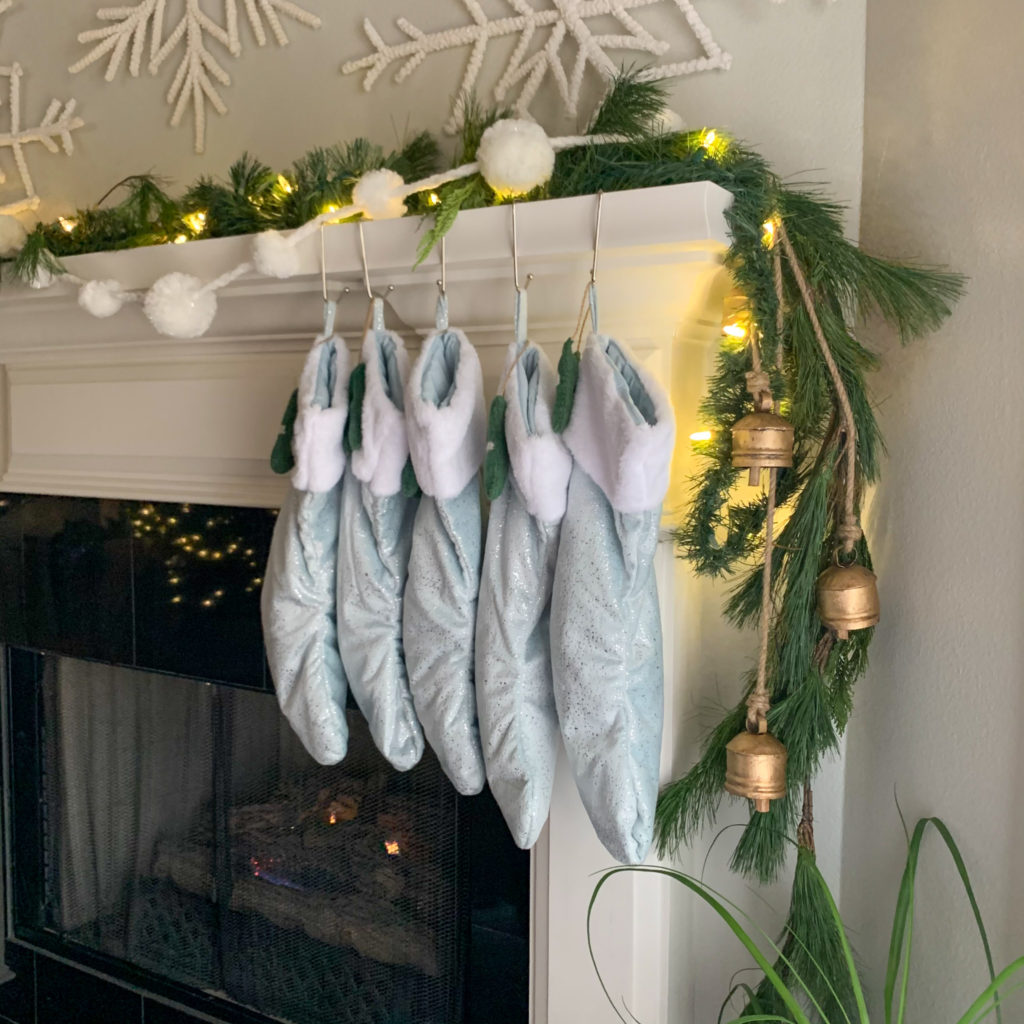 a Christmas mantel with blue and white Christmas decor including light blue stockings and vintage bells