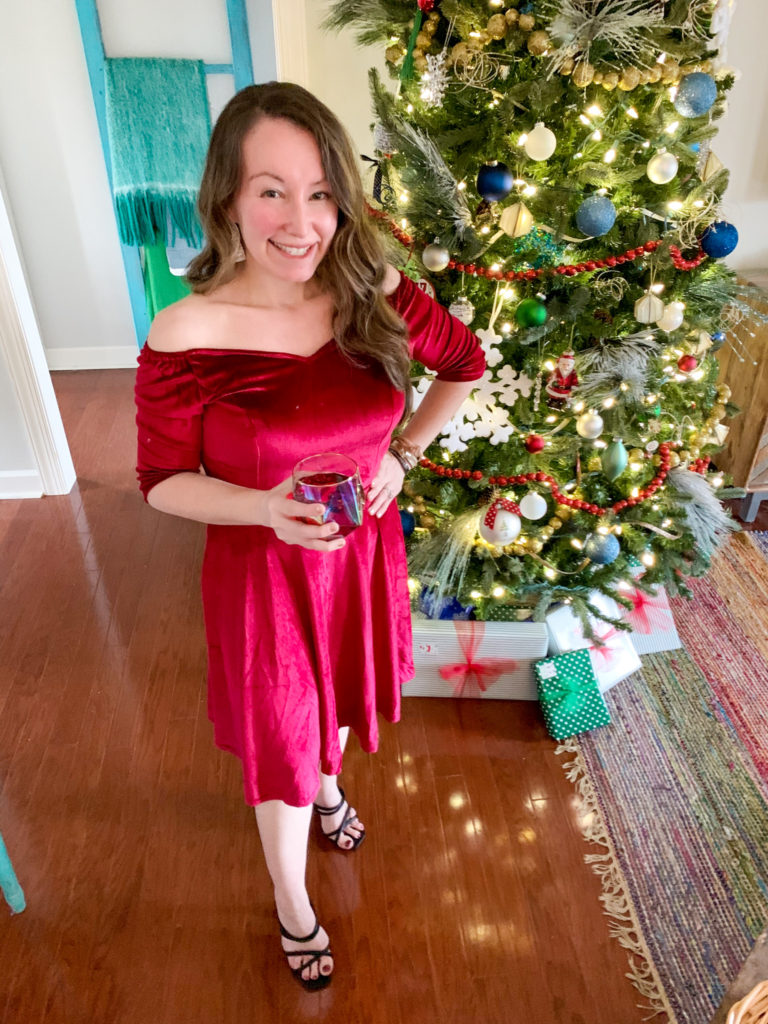 woman wears dress in front of Christmas tree with cocktail in hand