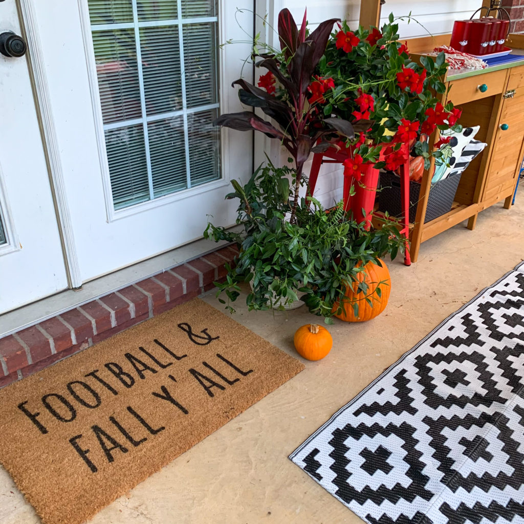 football and fall door mat with plants and pumpkins on back porch