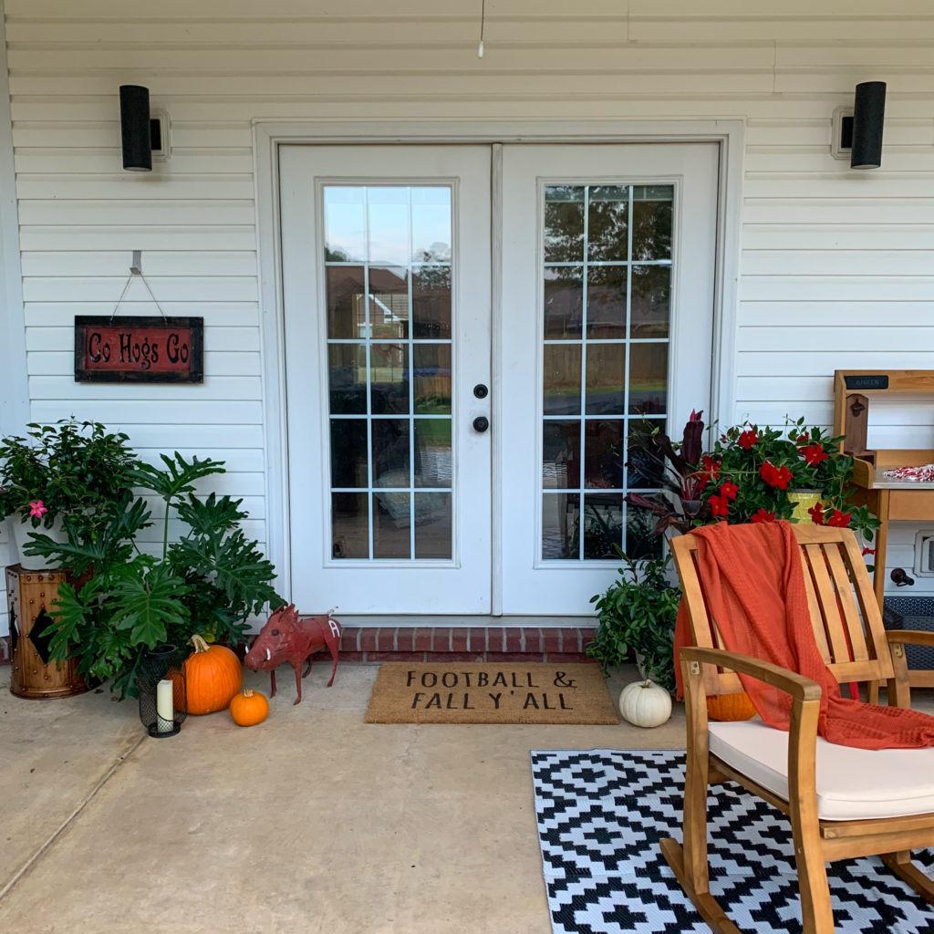 a fall football porch with a football and fall door mat, plants, and rocking chairs