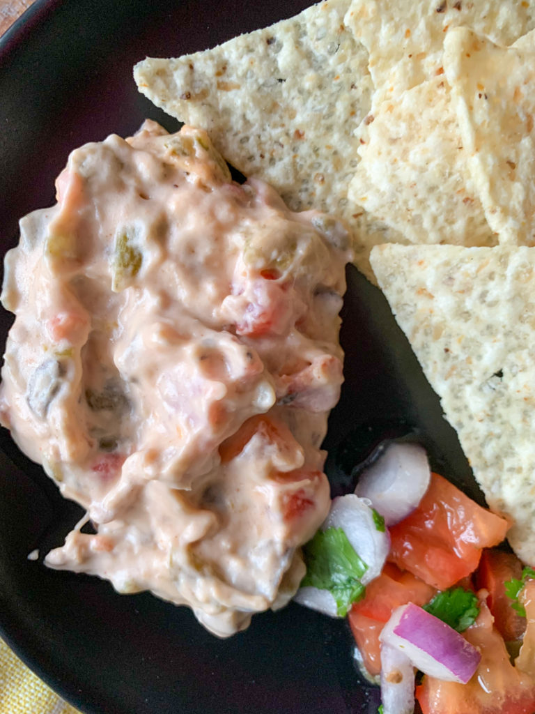 side scoop of green chile queso dip with pulled pork on black plate with pico de gallo and chips