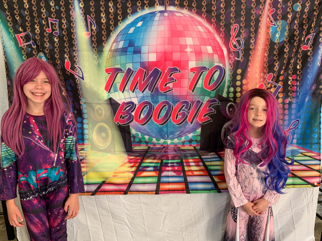 girls in Descendants costumes pose in front of a Time to Boogie banner