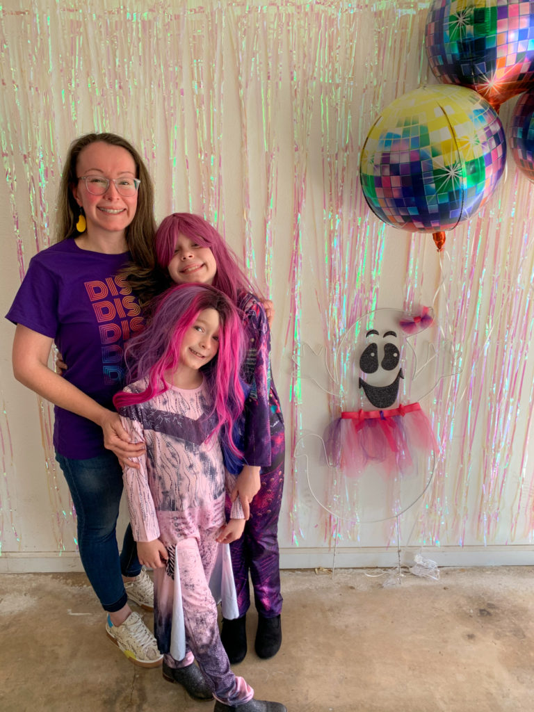 Arkansas lifestye blogger, Amy, poses with her children at their Halloween disco party with ghost and disco balls in back