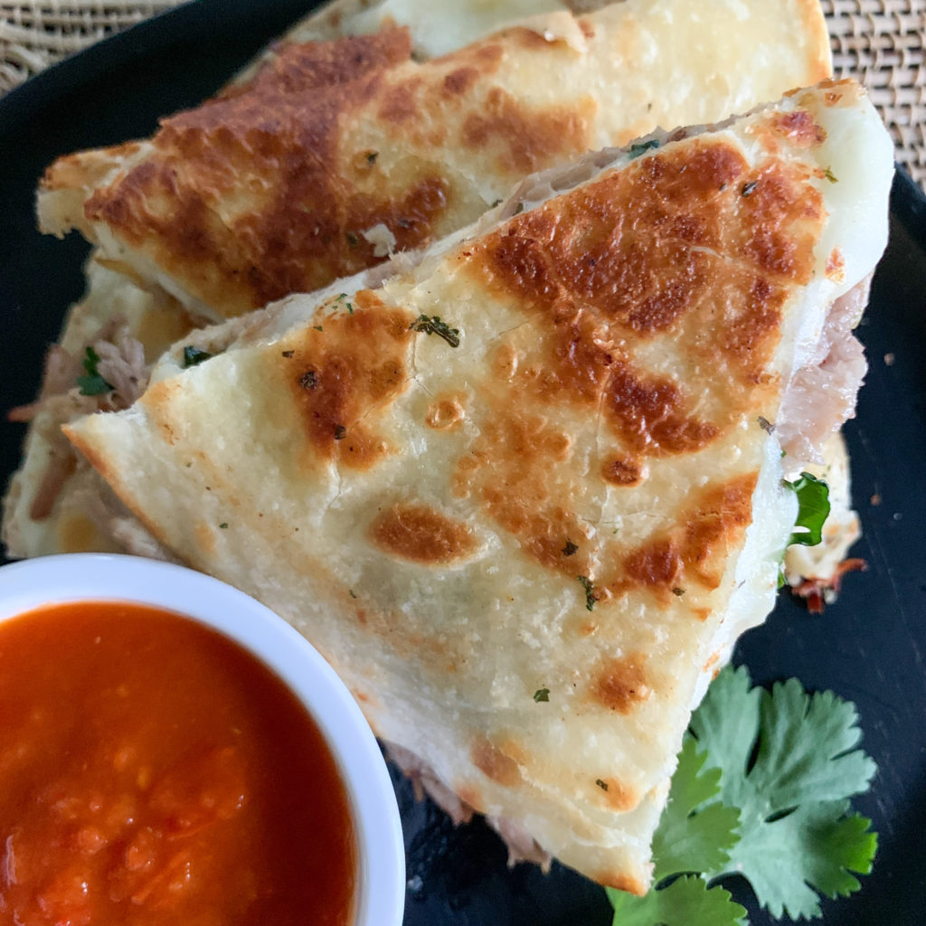 pulled pork quesadilla with Oaxaca cheese on black plate with salsa