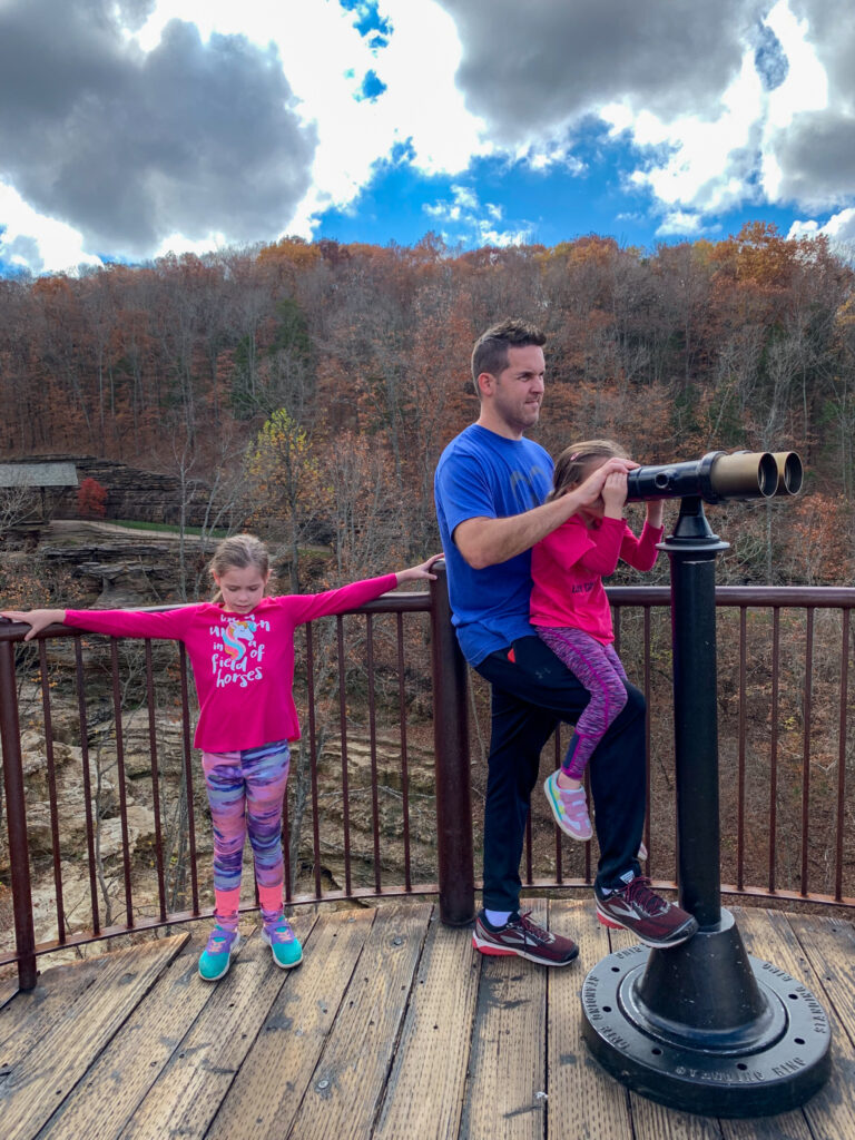 dad holds daughter to look in telescope at Top of the Rock