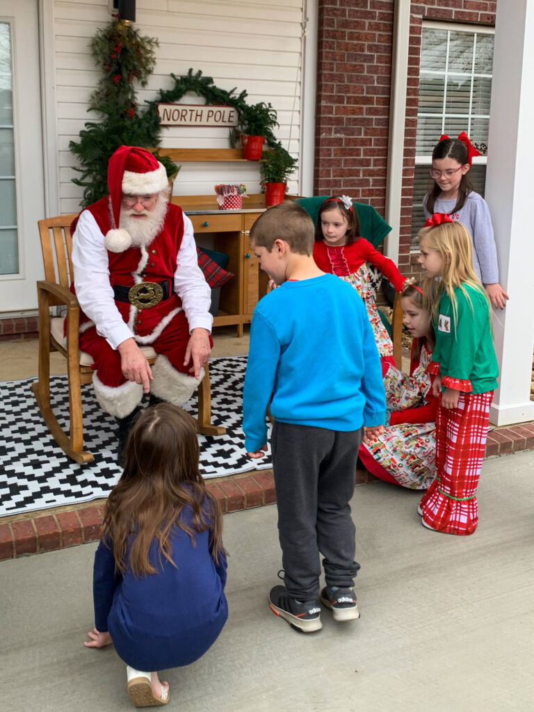 Santa visits with children on a back porch during a neighborhood Santa visit