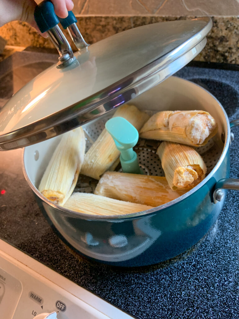 frozen tamales steaming in a blue pot over an adjustable steamer basket