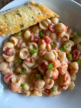 heaping pile of crawfish mac and cheese on white plate with garlic bread