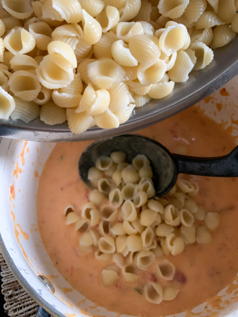 someone turns queso into mac and cheese by adding shell pasta to a pot of queso