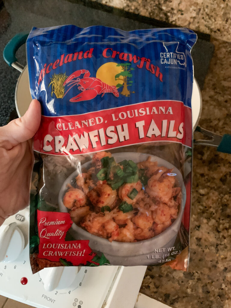 woman holds package of Riceland Crawfish tails over pot for a crawfish tails recipe