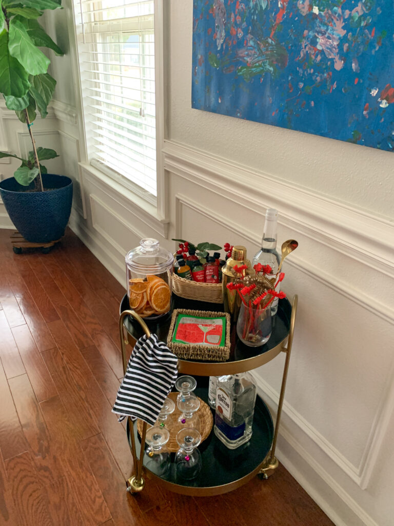 rolling gold drinks trolley with holiday bar accessories in dining room under blue painting