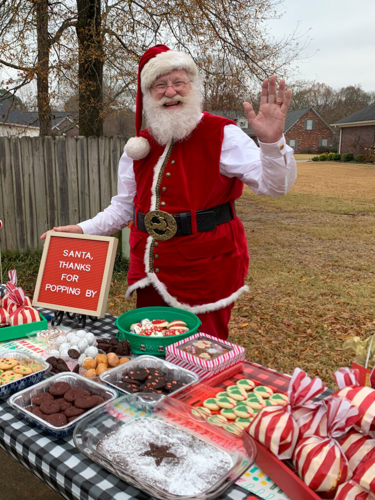 Santa Pete waves from behind a cookie table at a neighborhood Cookies with Santa event in Arkansas