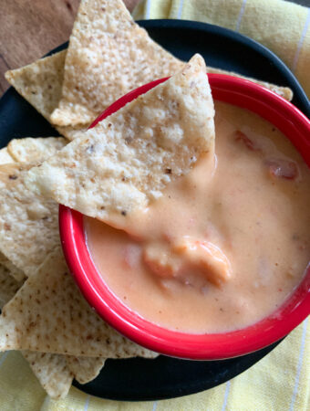 tortilla chip inside red bowl of spicy crawfish cheese dip