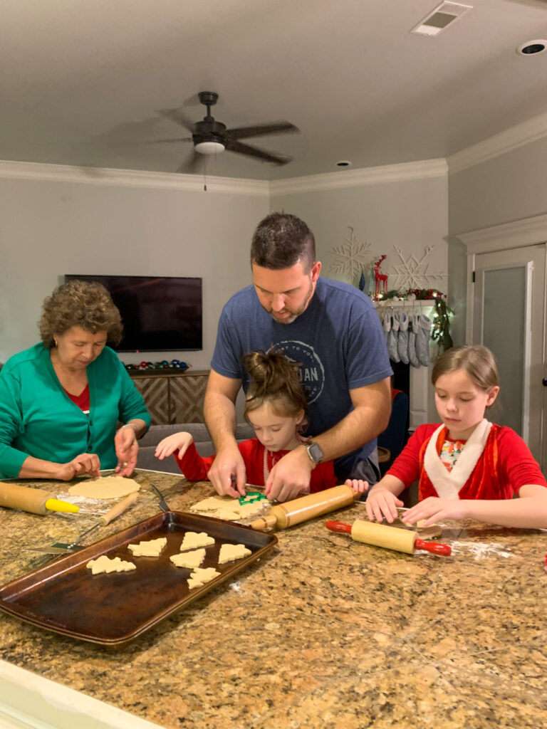 children making cookies with red and green sprinkles with their dad and grandma