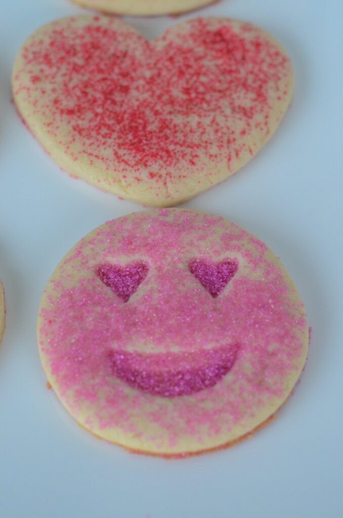red heart cookies and pink smiley face cookies on white plate - pink sugar cookies for Valentine's Day 