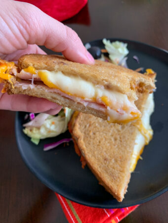 air fryer turkey and cheese sandwich in woman's hand over black plate