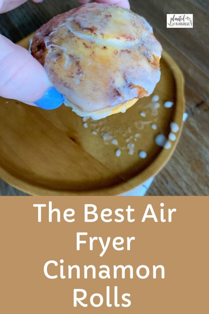 woman holds Pillsbury cinnamon roll in the air fryer over a brown plate