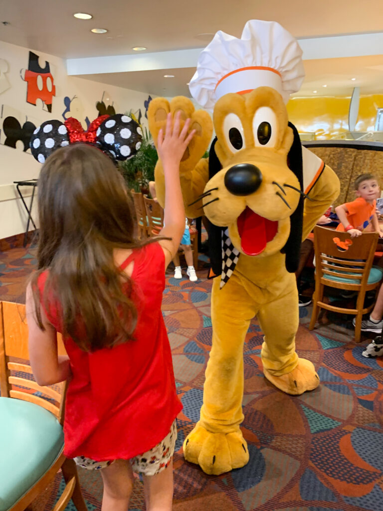 Pluto gives a girl a high five at Chef Mickey's breakfast