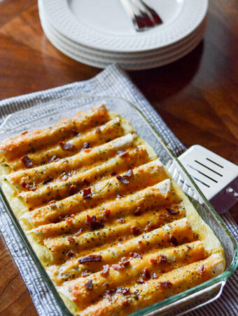 breakfast enchiladas with sausage in baking pan on cloth runner with spatula