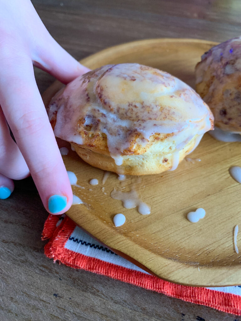 child's hand reaches for canned air fryer cinnamon rolls on brown plate