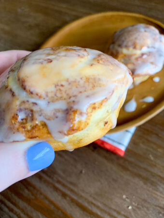 woman holding Pillsbury air fryer cinnamon roll above plate with napkin