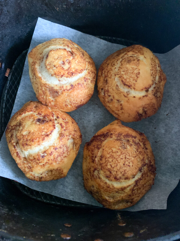 four air fryer cinnamon rolls in the air fryer basket on parchment paper