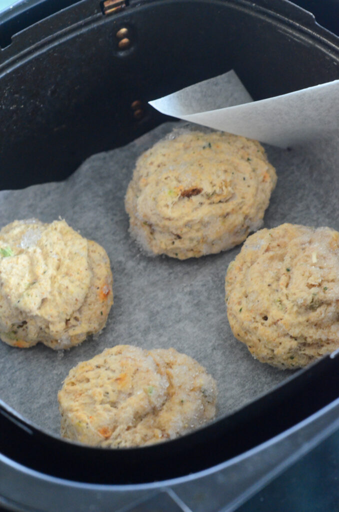 four frozen crab cakes in an air fryer on parchment paper