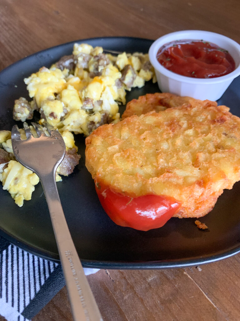 air fryer hash brown patties on black plate with eggs and ketchup 