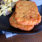 air fryer frozen hash browns on black plate with eggs and sausage