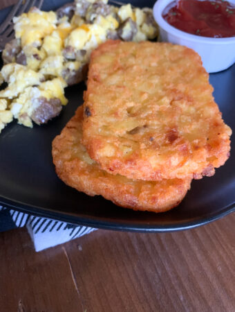 air fryer frozen hash browns on black plate with eggs and sausage