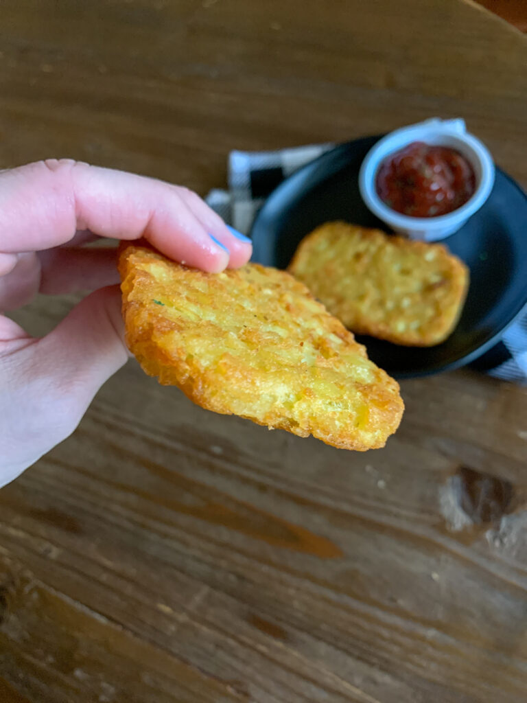 woman holds crispy air fryer potato patty in hand with plate in background