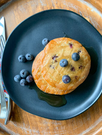 frozen pancakes in air fryer cooked and waiting on black plate with blueberries