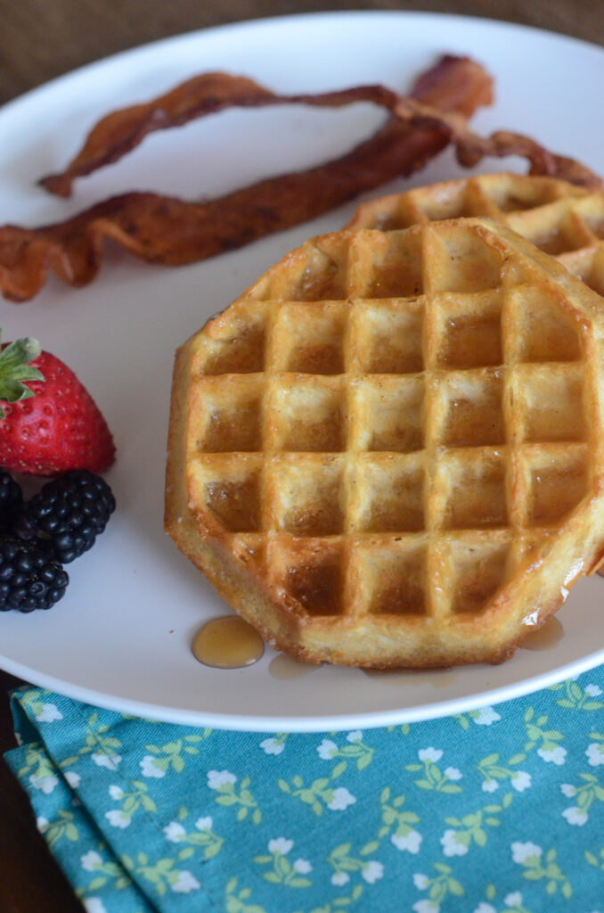 plate of air fryer frozen waffles with berries and bacon and a floral napkin in front