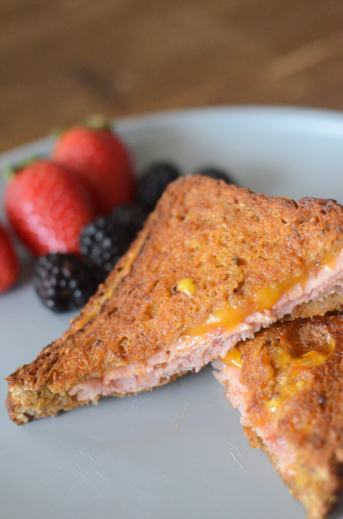 a hot grilled air fryer ham and cheese sandwich (air fryer ham melt) with fruit in back