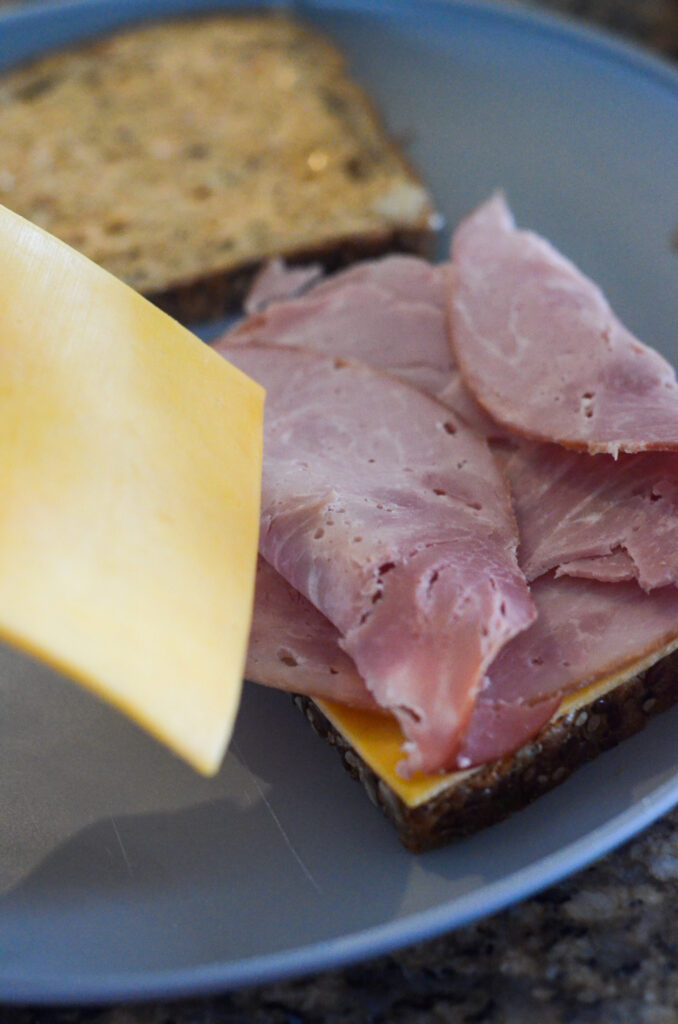 cheese going onto a pile of ham on a sandwich